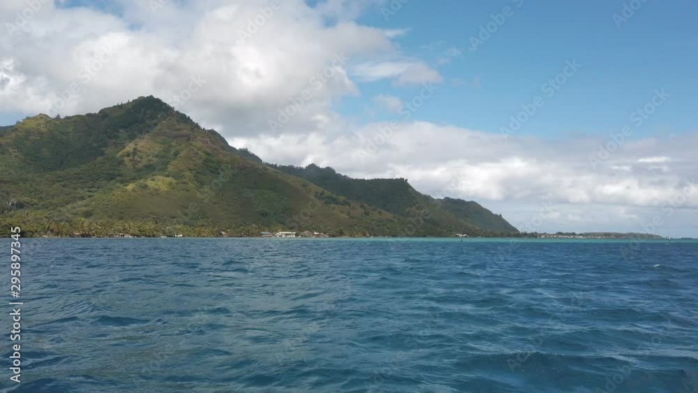 Stunning view of the Moorea landscape from sea. Bright blue water meets tall lush green mountains with a blue sky and soft white clouds. South Pacific island vacation paradise. Slow motion. Stunning view of the Moorea landscape from sea. Bright blue water meets tall lush green mountains with a blue sky and soft white clouds. South Pacific island vacation paradise. Slow motion.