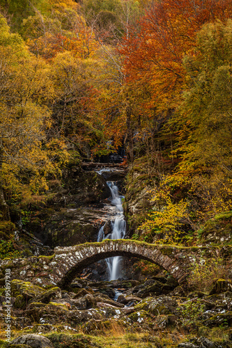 Stone bridge, waterfall and autumn foliage trees by the side of River Lyon in highland, Scotland UK