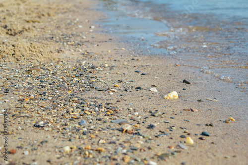 Sandy beach with pebble and coming waves at the sea, close-up