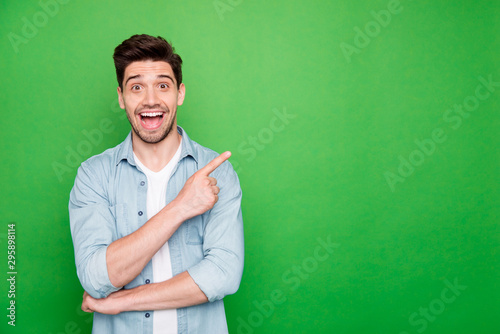 Photo of cheerful positive brown haired cute man pointing at empty space expressing shocked emotions excited ecstatic isolated over green vivid color background © deagreez