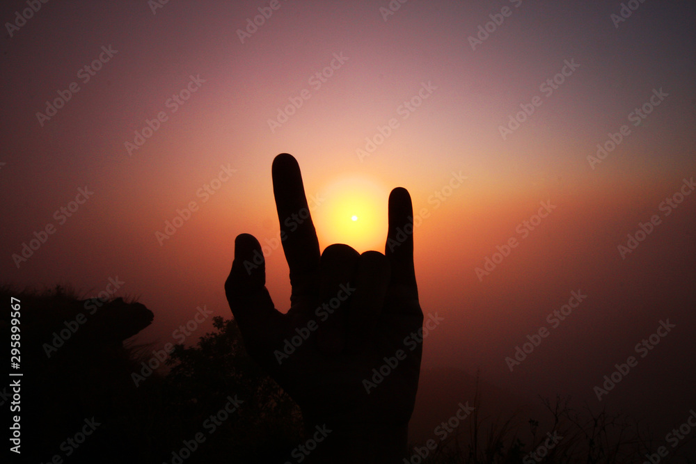 Beautiful silhouette of fingers and hand with valley of mountain in foggy and mist of sunrise shining on the sky