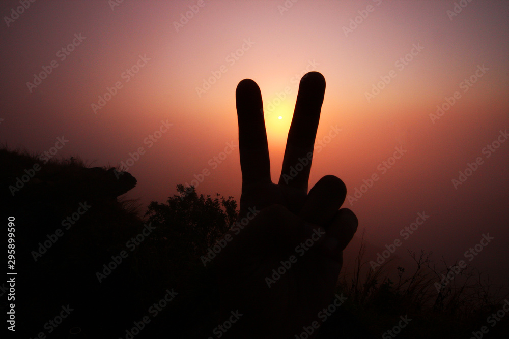 Beautiful silhouette of fingers and hand with valley of mountain in foggy and mist of sunrise shining on the sky