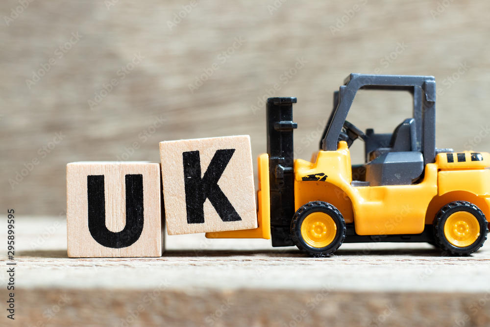 Toy forklift hold letter block k to complete word UK (abbreviation of united kingdom) on wood background - obrazy, fototapety, plakaty 