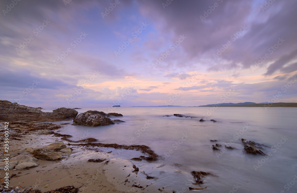 Obraz premium Mauve Sunset with wispy clouds on Pollan Beach, Inishowen, Ireland. Featuring rocks algues and sand with viiew of Malin Peninsula on horizon
