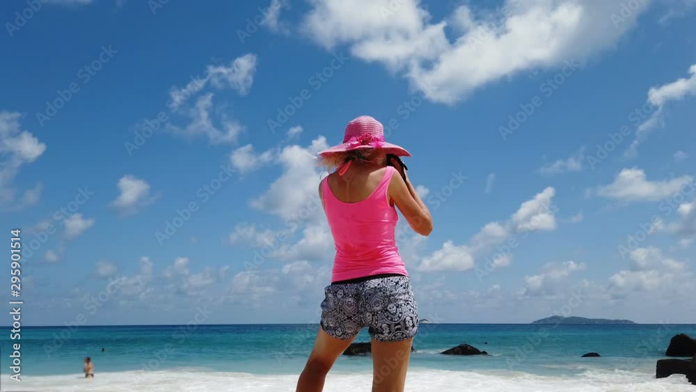 woman photographer with hat on a large granite boulder in popular and scenic Anse Lazio beach. Female lifestyle by turquoise waters of Indian ocean on Praslin Island, Seychelles. Summer holidays. woman photographer with hat on a large granite boulder in popular and scenic Anse Lazio beach. Female lifestyle by turquoise waters of Indian ocean on Praslin Island, Seychelles. Summer holidays.