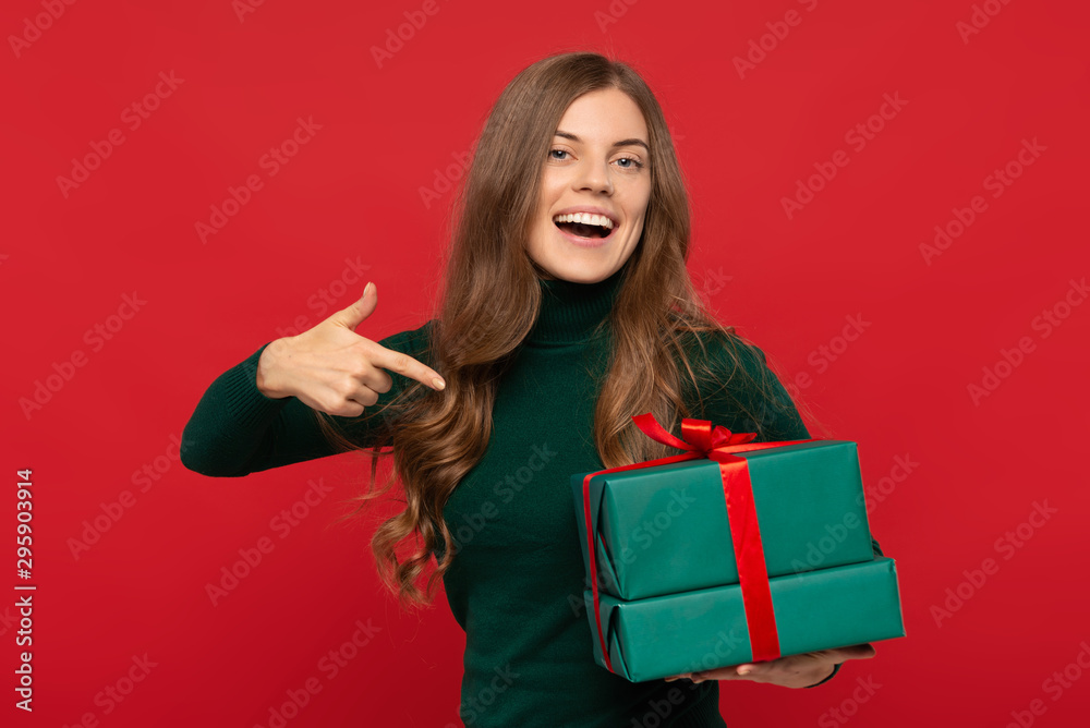 smiling woman in green sweater pointing on gift isolated on red background. Christmas concept smiling woman in green sweater pointing on gift isolated on red background. Christmas concept