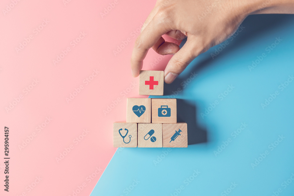 © oatawa - Health Insurance Concept, Hand of man arranging wood cube stacking with icon healthcare medical on pastel blue and pink background, copy space.