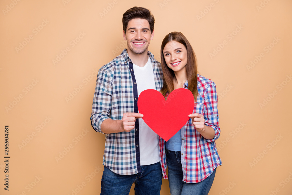 Portrait of romantic positive couple hold red paper card heart show symbol of their feelings wear checkered plaid casual style outfit isolated over pastel color background