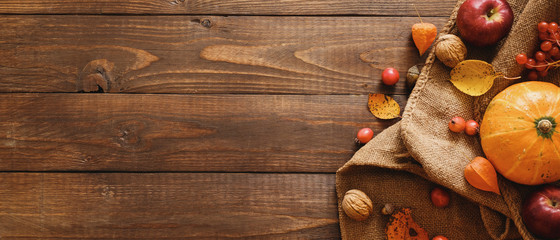 Harvest or Thanksgiving background with pumpkins, blanket, dried fall leaves, apples, red berries, walnuts on wooden table. Flat lay composition, top view, copy space