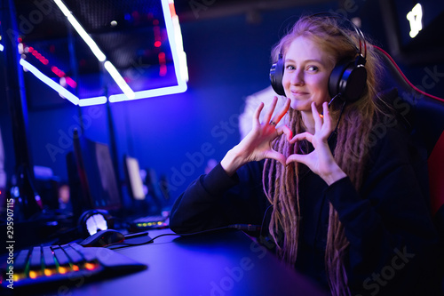 Streamer beautiful girl shows heart sign with hands professional gamer playing online games computer, neon color photo