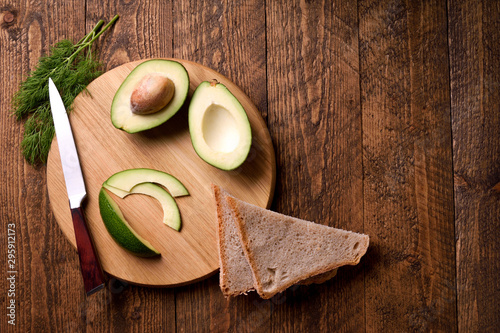 Beautifully plated avocado toast with delicious-looking toppings on wooden brouw background. Making sandwiches with avocado healthy organic food top view.On A Wooden Cutting Board Sliced avocado photo