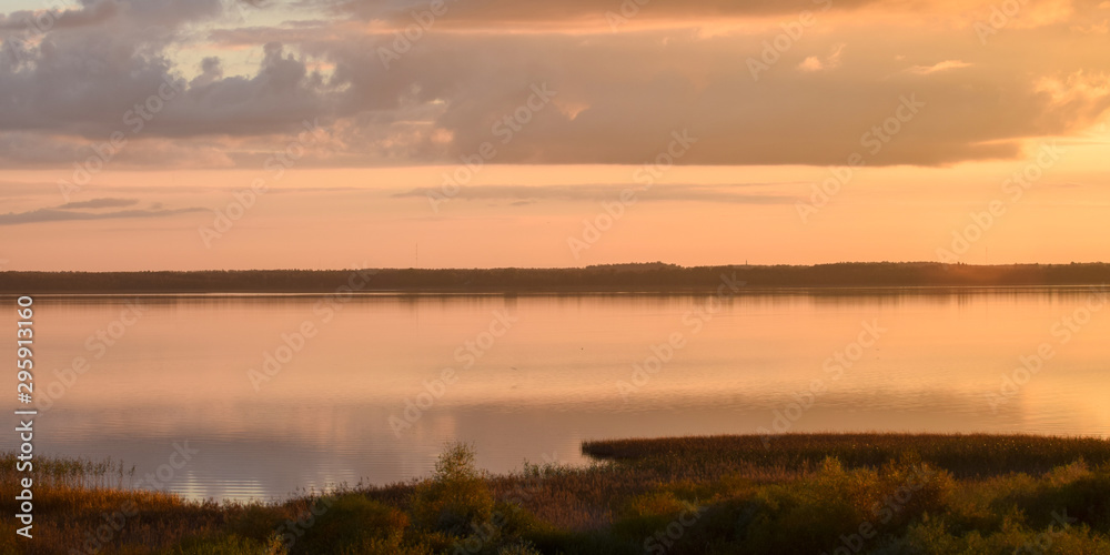 beautiful lake view evening with dark cloud moving above the lake with reflection on the water and colorful yellow sun light on the sky background, sunset