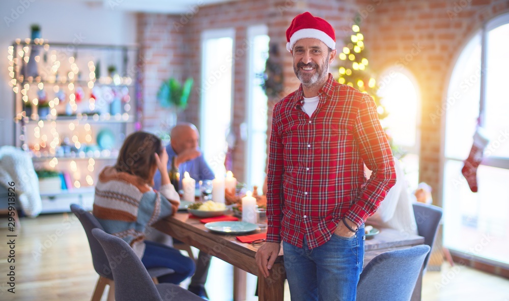 Middle age handsome man smiling happy and confident. Standing wearing santa hat celebrating Christmas with family at home
