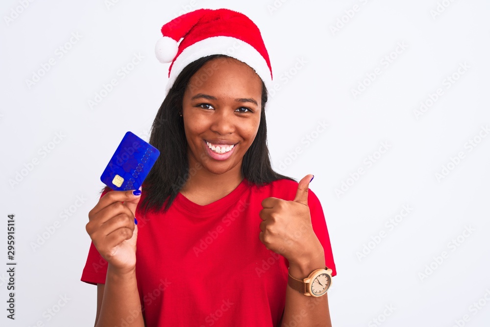 Young african american woman wearing christmas hat and holding credit card happy with big smile doing ok sign, thumb up with fingers, excellent sign Young african american woman wearing christmas hat and holding credit card happy with big smile doing ok sign, thumb up with fingers, excellent sign