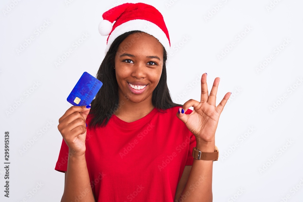 Young african american woman wearing christmas hat and holding credit card doing ok sign with fingers, excellent symbol Young african american woman wearing christmas hat and holding credit card doing ok sign with fingers, excellent symbol