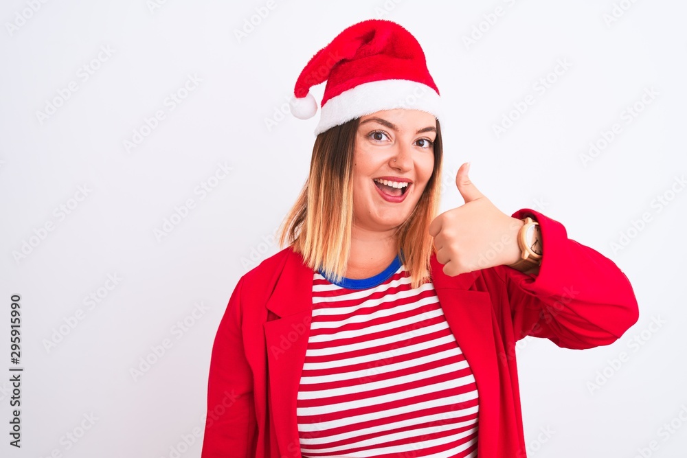Young beautiful woman wearing Christmas Santa hat over isolated white background doing happy thumbs up gesture with hand. Approving expression looking at the camera with showing success. Young beautiful woman wearing Christmas Santa hat over isolated white background doing happy thumbs up gesture with hand. Approving expression looking at the camera with showing success.