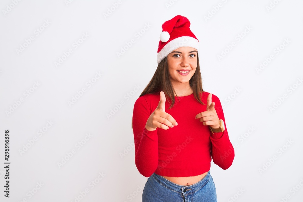 Young beautiful girl wearing Christmas Santa hat standing over isolated white background pointing fingers to camera with happy and funny face. Good energy and vibes.