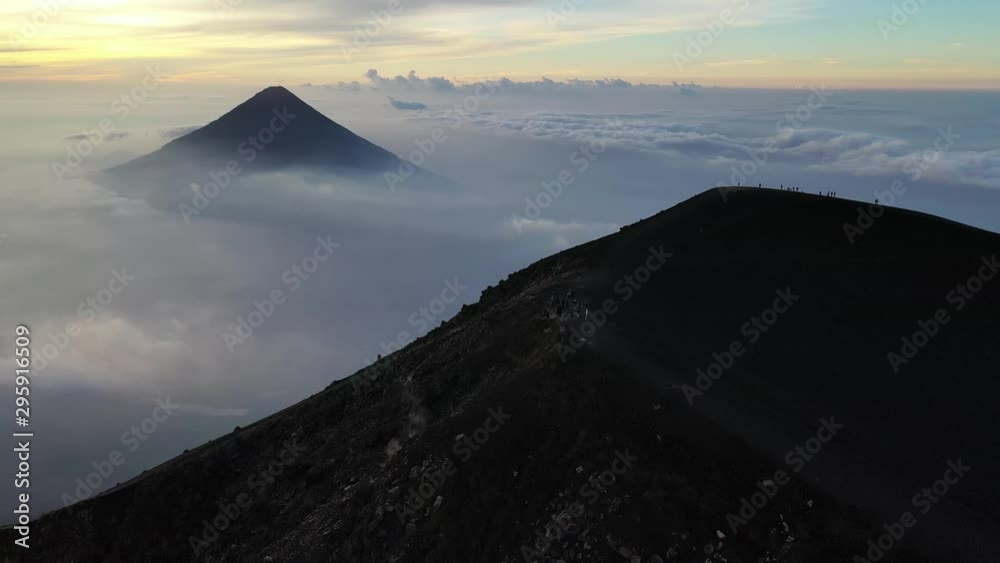 Guatemala volcano Acatenango and volcano Fuego aerial drone 4K video. Beautiful sunrise at the top of the volcano Acatenango surrounded by clouds. Hikers standing at the top of the mountain.