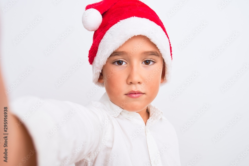 Beautiful kid boy wearing Christmas Santa hat make selfie over isolated white background with a confident expression on smart face thinking serious Beautiful kid boy wearing Christmas Santa hat make selfie over isolated white background with a confident expression on smart face thinking serious