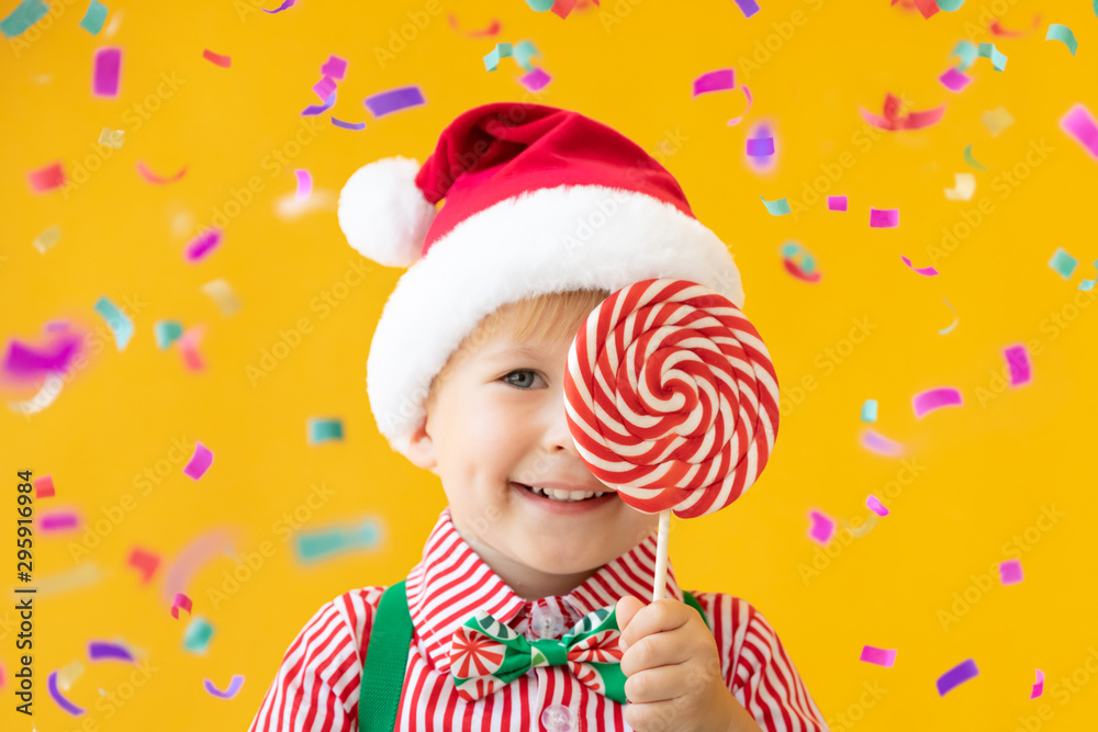 Happy child holding lollipop in hand against yellow background