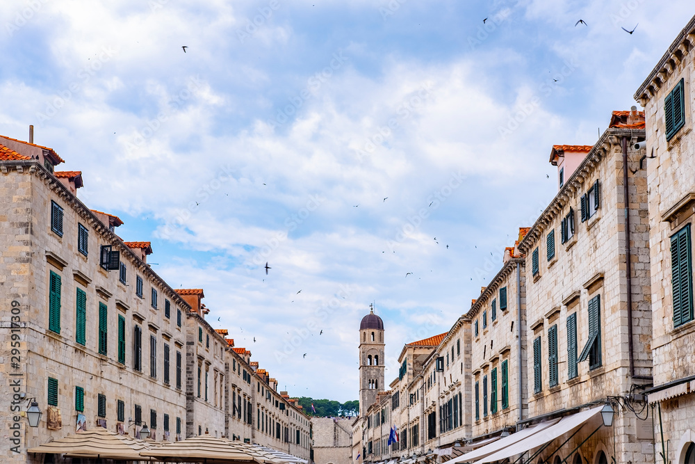 Stone houses, facades in Stradun street (Placa) and blue sky with birds, main street in old historic Dubrovnik city, Dalmatia, Croatia