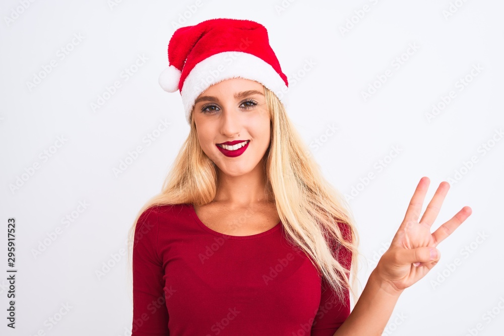 Young beautiful woman wearing Christmas Santa hat over isolated white background showing and pointing up with fingers number three while smiling confident and happy. Young beautiful woman wearing Christmas Santa hat over isolated white background showing and pointing up with fingers number three while smiling confident and happy.