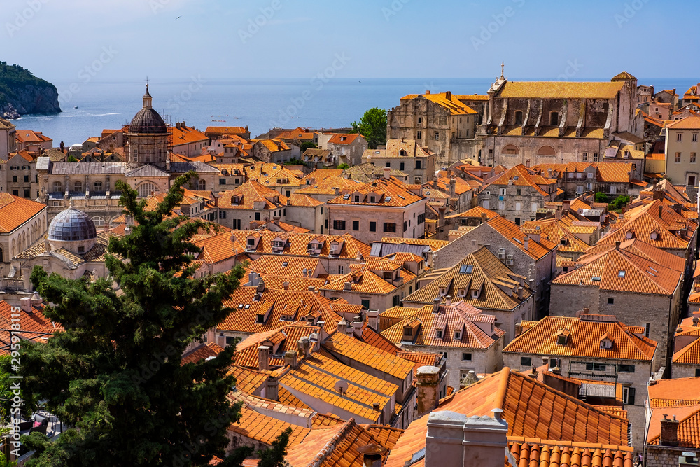Old stone houses with red roofs in old historic Dubrovnik city, blue Adriatic Sea on sunny summer day, green tree, Dalmatia, Croatia, the most popular touristic destination