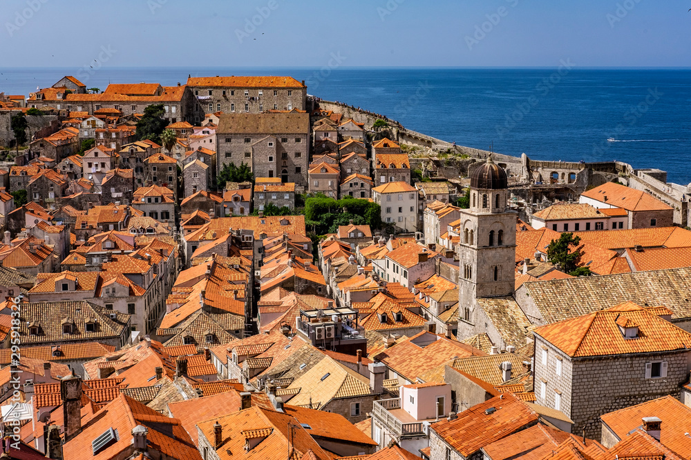 Bell tower with old stone houses with red roofs in old historic Dubrovnik city, Dalmatia, Croatia, blue summer day and blue Adriatic Sea, the most popular touristic destination