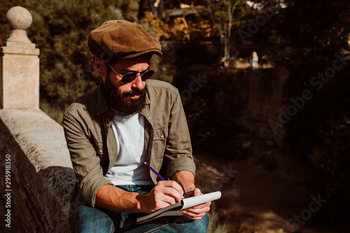 .Young man sitting in the street of Granada, Spain, drawing in his travel notebook. Enjoying the sunset, developing his creativity. Relaxed and carefree. Lifestyle.