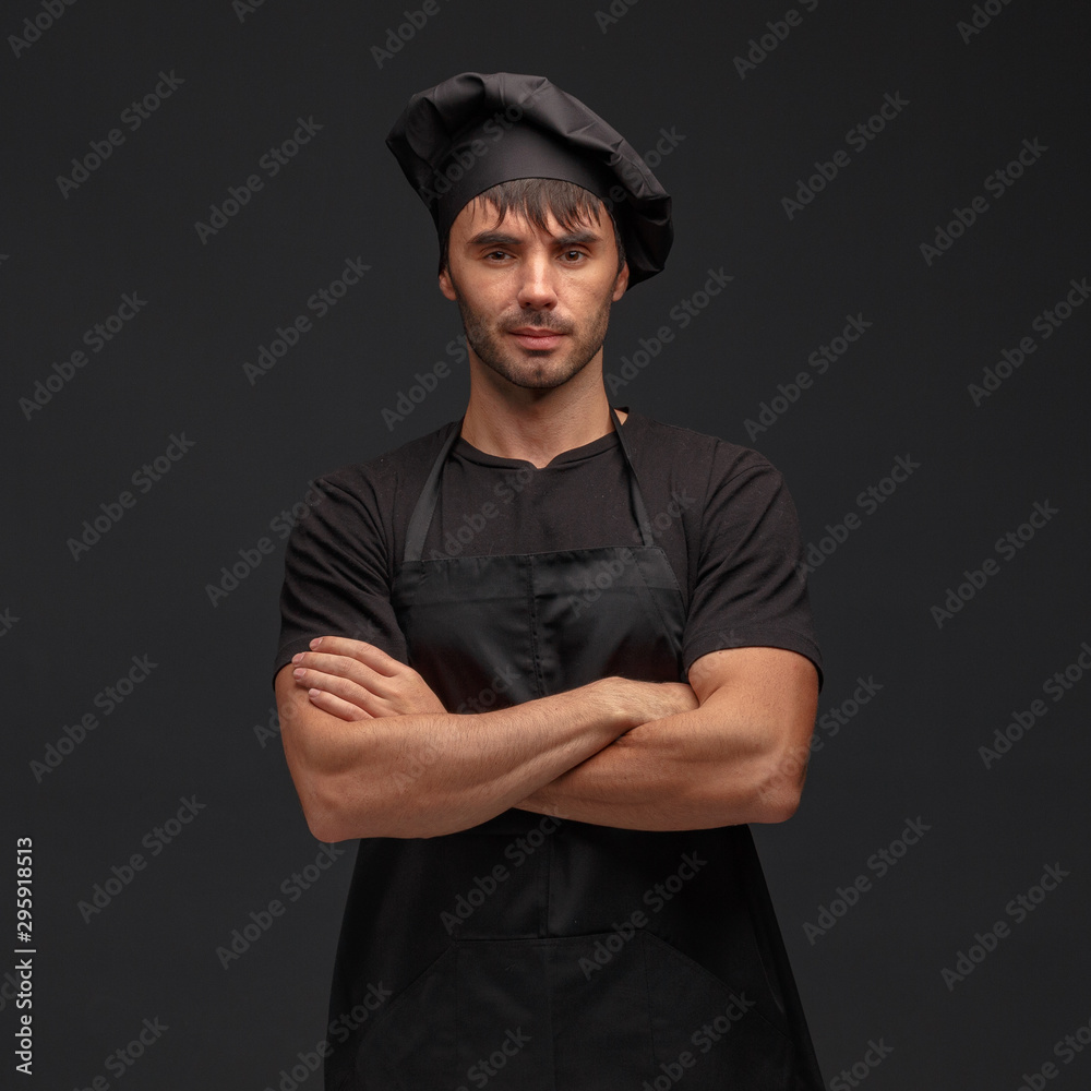 Young male cook in a black apron and hat.