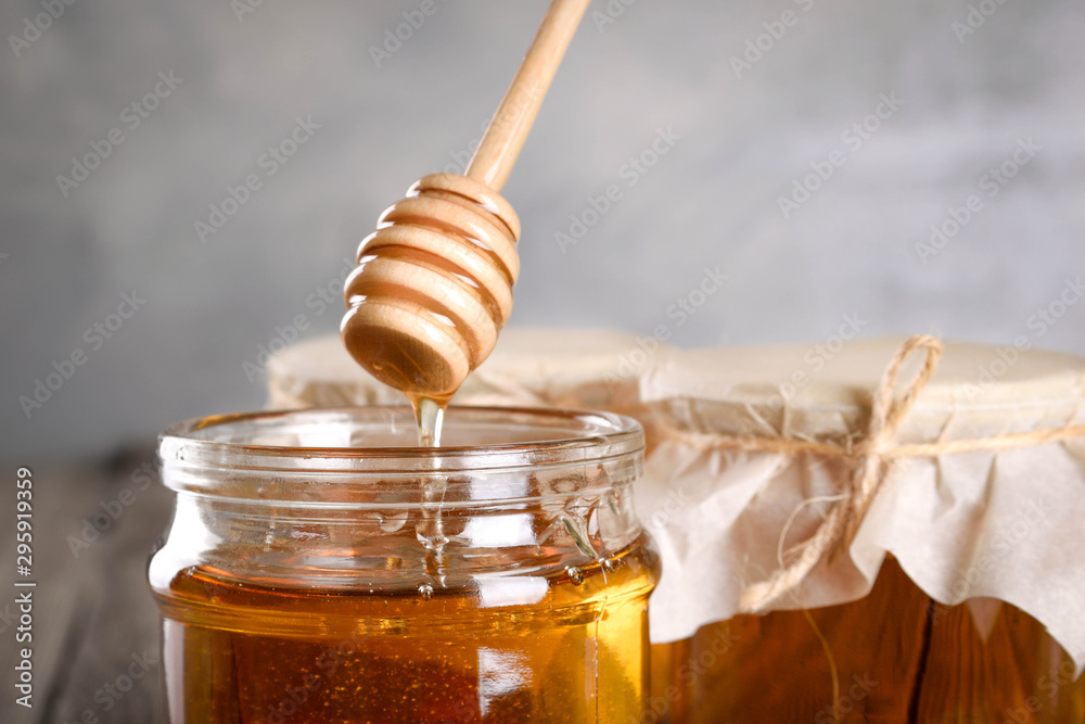 Pouring aromatic honey into jar, closeup. Honey in glass jars and honeycombs wax on wooden background. Wooden stick , instruments Pouring aromatic honey into jar, closeup. Honey in glass jars and honeycombs wax on wooden background. Wooden stick , instruments