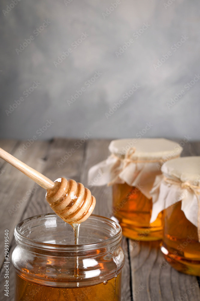 Pouring aromatic honey into jar, closeup. Honey in glass jars and honeycombs wax on wooden background. Wooden stick , instruments Pouring aromatic honey into jar, closeup. Honey in glass jars and honeycombs wax on wooden background. Wooden stick , instruments