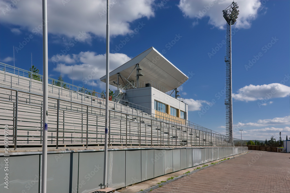 Empty stadium stands against a background of blue sky and white clouds.