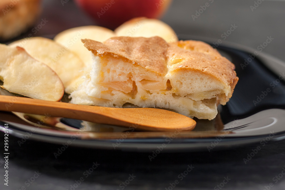 Slice Charlotte apple pie on a black plate with a wooden spoon on a black wooden table.Close up. Slice Charlotte apple pie on a black plate with a wooden spoon on a black wooden table.Close up.