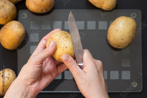 top view of woman hand peeling raw potato with knife on black background
