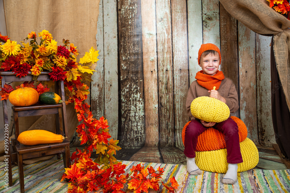 a boy in an orange scarf and hat sits with a pumpkin