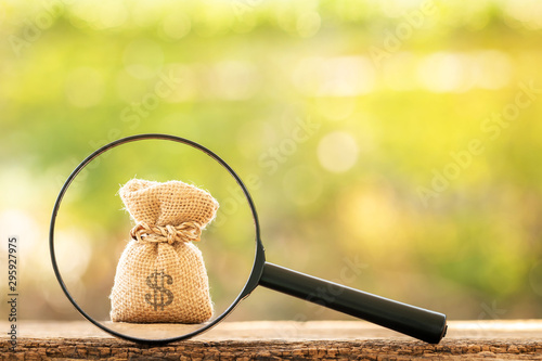 Magnifying glass with searching for money bag put on the wood on bokeh background, Loan and find for business investment fund  in the future concept. photo