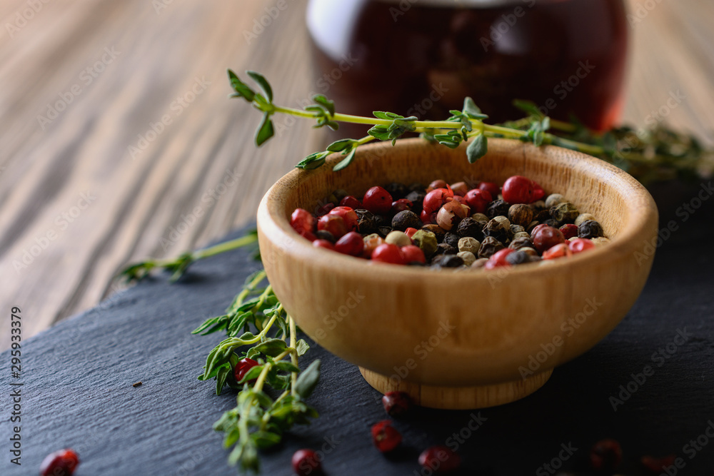 A mix of different peas of peppers in red, black, white, green in a wooden bowl next to sprigs of thyme and wine vinegar are ready for cooking eat A mix of different peas of peppers in red, black, white, green in a wooden bowl next to sprigs of thyme and wine vinegar are ready for cooking eat