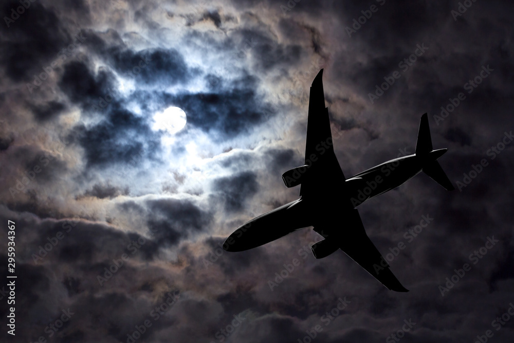 Full moon and silhouette passenger plane on  cloudy sky background. Danger of a airplane crash in bad weather. Dramatic Halloween night. Airliner makes a night flight in stormy weather.