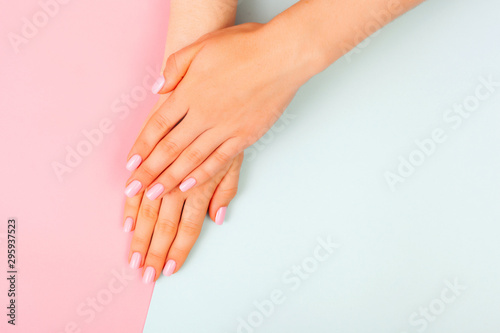 Stylish trendy female pink manicure. Beautiful young woman s hands on pink and blue pastel background.