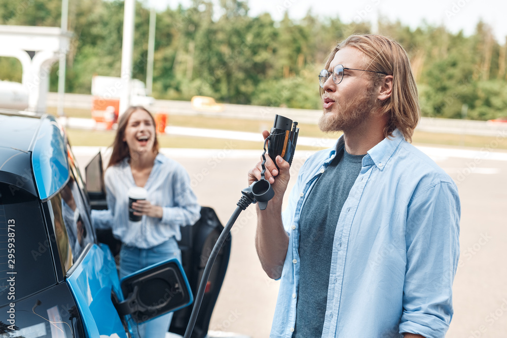 Young adult man holding power cable supply for charging electric car Young adult man holding power cable supply for charging electric car