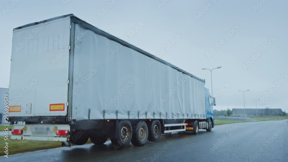 Long Haul Semi-Truck with Cargo Trailer Full of Goods Travels on the Highway Road. Daytime Driving Across Continent Through Rain, Fog. Industrial Warehouses Area. Back View Following Shot Long Haul Semi-Truck with Cargo Trailer Full of Goods Travels on the Highway Road. Daytime Driving Across Continent Through Rain, Fog. Industrial Warehouses Area. Back View Following Shot