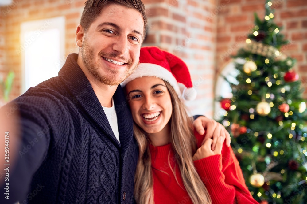 Young beautiful couple smiling happy and confident. Standing make selfie by camera around christmas tree at home Young beautiful couple smiling happy and confident. Standing make selfie by camera around christmas tree at home
