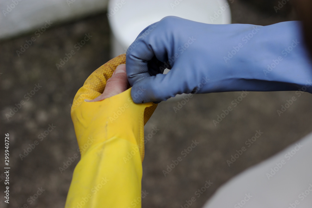 Man is doing chores around the house with yellow and blue gloves. Used broken yellow grove showing off the thumb. Taking the trash out from the bin. Taking off the tore glove from the left hand.