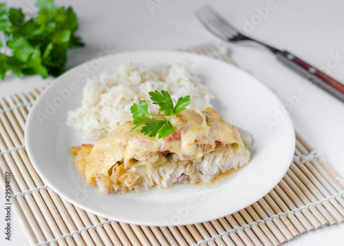 Baked fish with cheese, tomatoes and rice on a white plate. Sea catfish. close-up