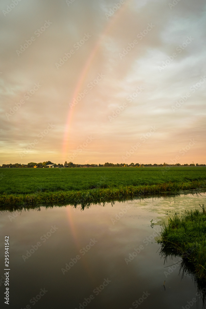 Rainbow over the countryside of Holland with reflection in calm water Rainbow over the countryside of Holland with reflection in calm water