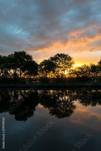 Beautiful sunrise over the calm water of the river Gouwe in the Netherlands. Trees are silhouetted against the colorful sky.