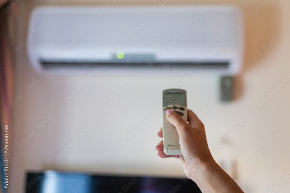 In female hands of the remote control air conditioning in the hotel room. Cooling and airing in the hotel room. Close-up view of the use of some electrical appliances such as air conditioning.