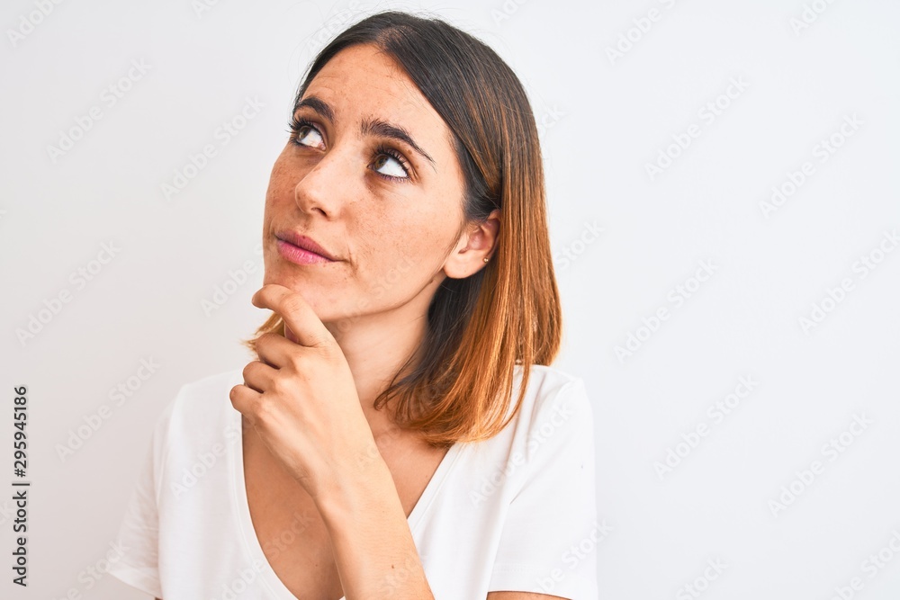 Beautiful redhead woman wearing casual white t-shirt over isolated background serious face thinking about question, very confused idea Beautiful redhead woman wearing casual white t-shirt over isolated background serious face thinking about question, very confused idea