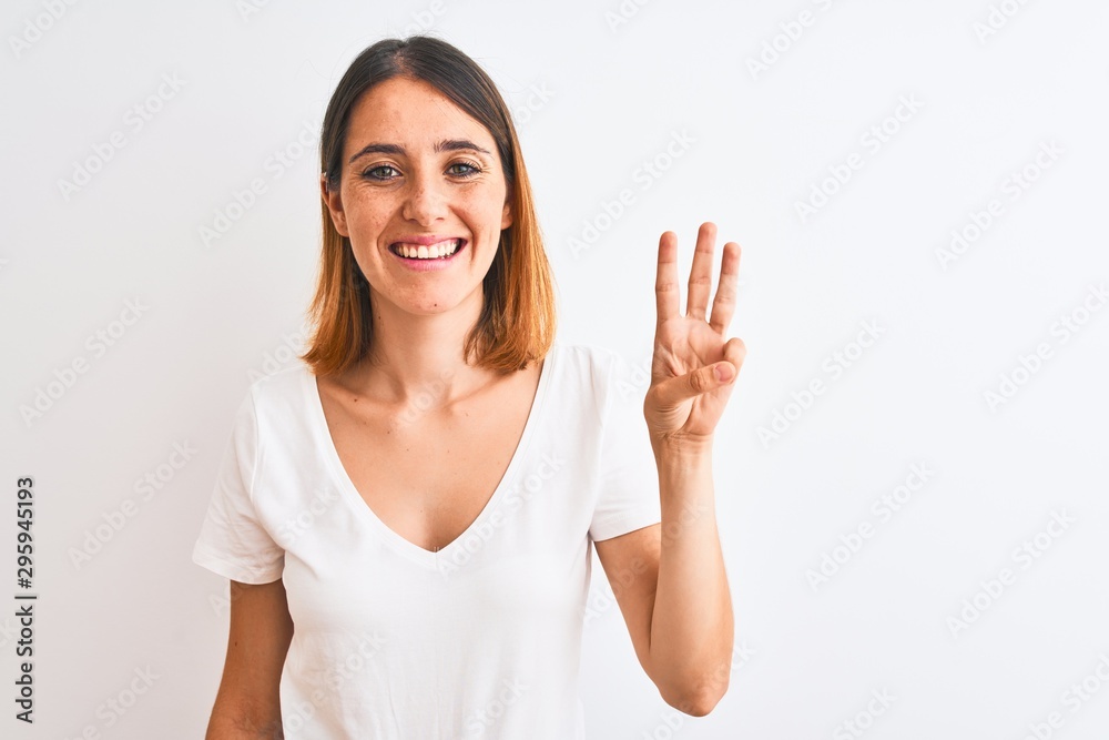 Beautiful redhead woman wearing casual white t-shirt over isolated background showing and pointing up with fingers number three while smiling confident and happy. Beautiful redhead woman wearing casual white t-shirt over isolated background showing and pointing up with fingers number three while smiling confident and happy.